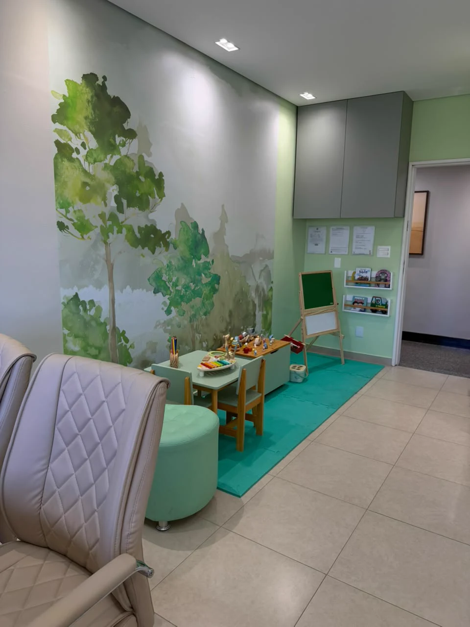 Sala de espera do consultório da Dra. Roberta, com mesinha de brinquedos, quadro-negro e pé de árvore pintado na parede